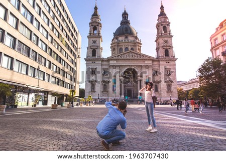 Young couple take pictures of each other while standing in front of St. Stephens Basilica in Budapest, Hungary