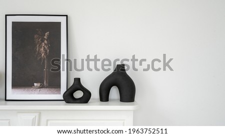 Home decor concept. Panoramic view of elegant black vase and mockup picture in frame on shelf above fireplace. New apartment with contemporary interior design and white copy space wall