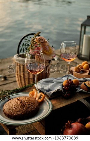 A romantic al fresco dinner overlooking the water. Close-up of two glasses of champagne, pastries and fruits in the light of the setting sun.