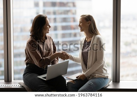 Smiling female colleagues shake hands get acquainted greeting after negotiations in office. Happy businesswomen handshake closing deal or making agreement at casual meeting. Partnership concept. Royalty-Free Stock Photo #1963784116