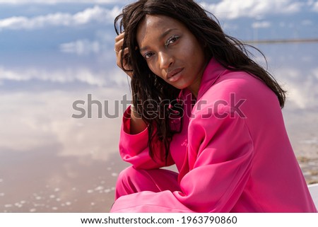 Mixed race beautiful woman portrait. Looking at camera. Pink bright suit. Nature sky with clouds background. expressive look with glitter makeup. Fashion mood summer sun colors