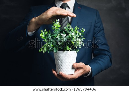 young businessman holding a vase with plants on a dark background