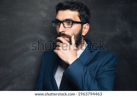 young businessman stands and thinks with his hand to his chin on a dark background