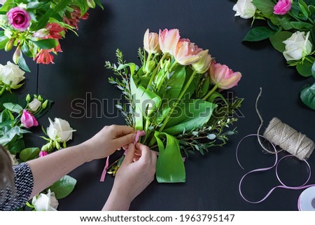 The florist arranging the bouquet. The hands of a young white woman. Fresh flowers: tulips, roses. Arranging a bouquet in a flower shop. Small business.