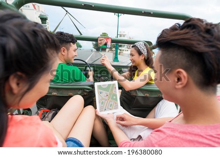 Girl taking a picture of the car driver while her friends on the backseat are using tablet with navigator on the screen