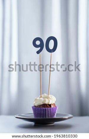 Homemade chocolate tasty cupcake with creamy topping and number 90 ninety on black plate and bright background. Anniversary minimalistic greeting card concept. High quality vertical image