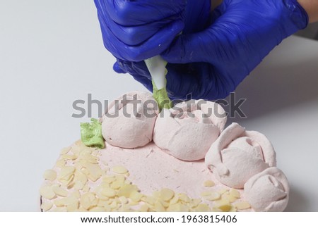 A woman prepares a marshmallow cake. Makes green leaves on roses from marshmallows. Works with a mask and gloves.