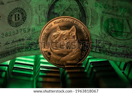 Doge cryptocurrency physical coin placed next to US dollar in the dark background and lit with green light Royalty-Free Stock Photo #1963818067