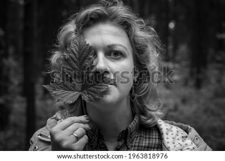 The blonde woman covers her eyes with green leaves. Black and whait photo.