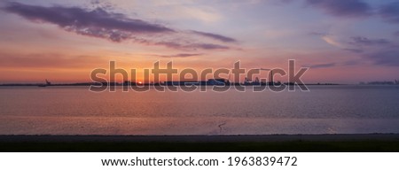 panorama picture of a scenic sunset over the river Weser with silhouettes of the skyline of the industrial area Nordenham-Blexen - seen from Bremerhaven (Germany)