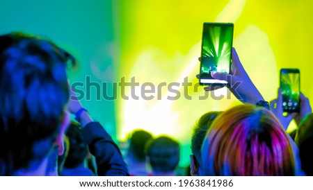 Teenagers hands taking photo or recording video of live music concert with smartphone. Crowd partying in front of stage. Photography, entertainment, technology concept