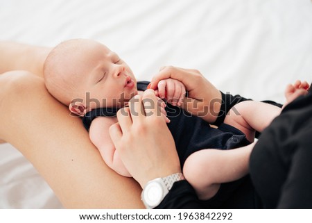 newborn baby in black bodysuit yawns lying on mom's legs