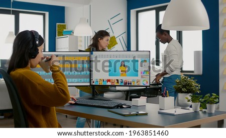 Graphic editor retouching photos of a client on performance PC with two displays setup. Woman retoucher working in photo editing software app sitting in creative agency office holding stylus pen