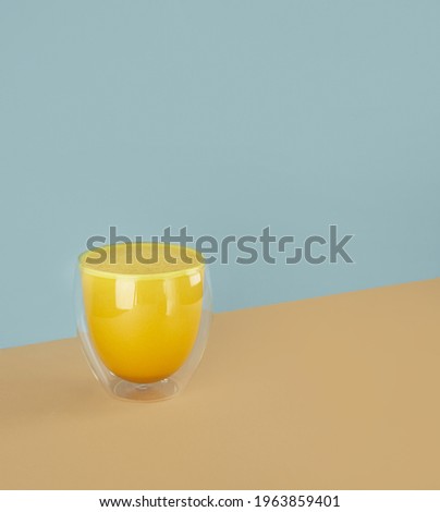 Golden yellow milk with turmeric in a glass on a isometric diagonal projection blue and beige background. healthy natural energy drink. Concept turmeric latte. Vertical. Copy space.