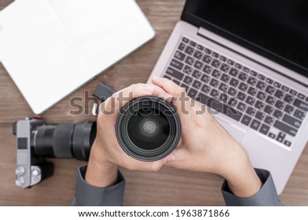 Close up camera lens in hand a man and photography equipment on vintage wood table : photo work concept