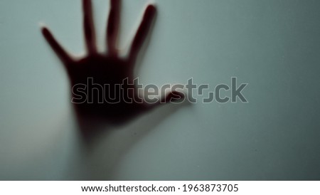 Marco hand waving behind frosty glass. Female fingers sliding on glass surface indoors. Abstract defocused woman hand making fist in smoggy studio. Disappearing blurred fist in horror scene. Royalty-Free Stock Photo #1963873705