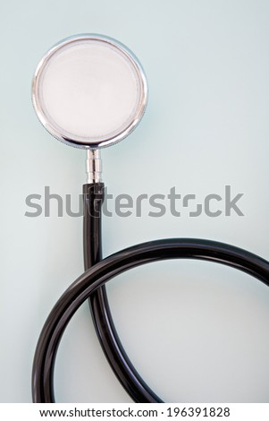 Close up detail still life view of a doctor stethoscope laying on a plain blue background space on a hospital table, interior. Health, clinical and medical equipment and insurance icon with no people.