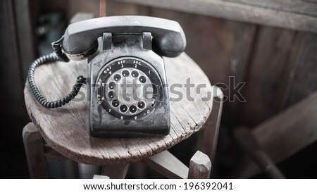 Vintage black phone on old wooden chair background ,retro filter effect