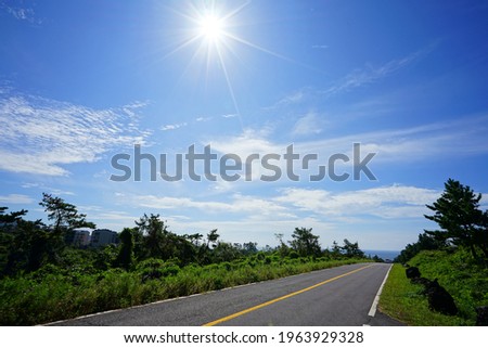 a road to the sea, with the sun and clouds