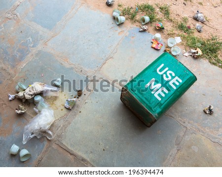 A bin put down on the floor with rubbish all over the place in India.