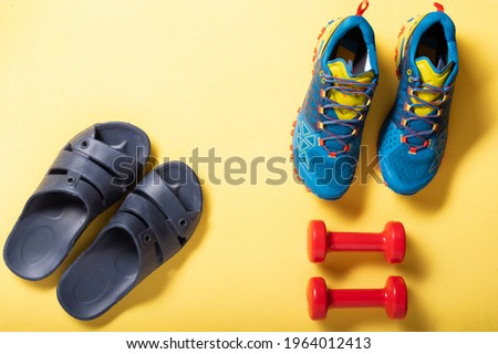 Home slippers and sports shoes. Sports shoes and dumbbells on a yellow mat. Top.