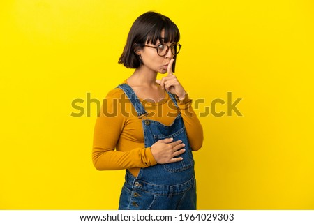 Young pregnant woman over isolated yellow background showing a sign of silence gesture putting finger in mouth
