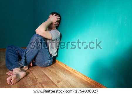 Alone man covers his head and face with his hands. Sitting on the floor in an empty green room. Psychological problems or a bad head concept.