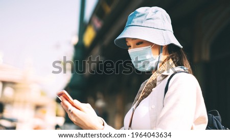 Young adult asian woman backpack traveller wear face mask for corona virus or covid-19. Female using mobile phone applicaiotn. People traveling in city lifestyle at outdoor. Bangkok, Thailand