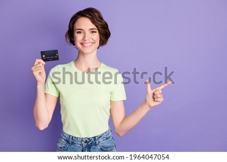 Portrait of lovely cheerful girl holding in hands bank card demonstrating aside copy space ad isolated over violet color background
