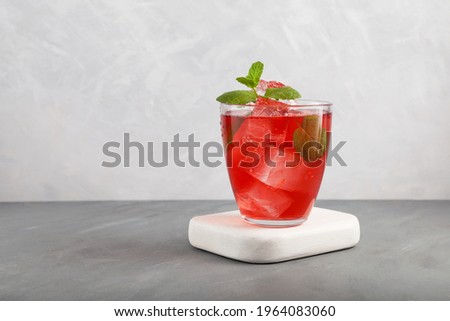 Iced fruit tea or cold watermelon drink in clear glass with mint leaf. Refreshing summer drink. Grey background, copy space. 