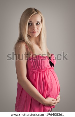 pretty pregnant woman wearing pink dress and holding hand on belly. on grey background