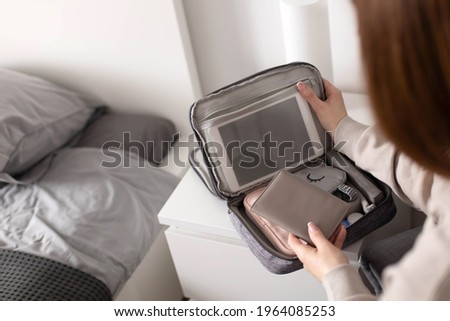 Female hands putting tablet pc into comfortable bag storage get ready to business trip or vacation. Woman packing wires, charge, powerbank modern devices to case. Beautiful comfy organization Royalty-Free Stock Photo #1964085253