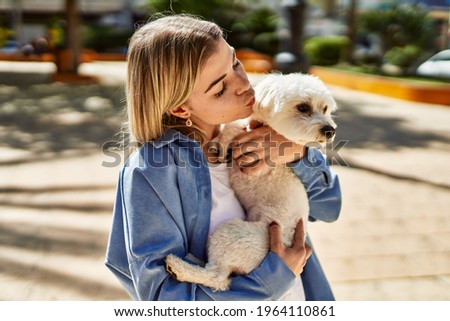 Young blonde girl kissing dog at the city.