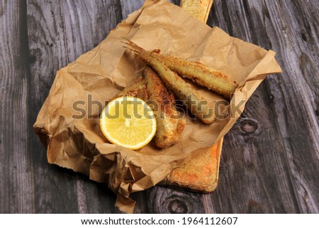 fried breaded fish served on paper, decorated with fresh lemon, old wood background. horizontal view from above 