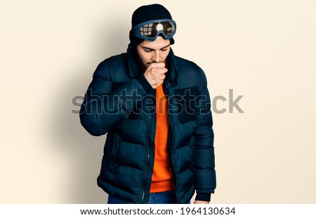 Young hispanic man with beard wearing snow wear and sky glasses feeling unwell and coughing as symptom for cold or bronchitis. health care concept.  Royalty-Free Stock Photo #1964130634