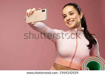 Cheerful young woman with yoga mat making selfie