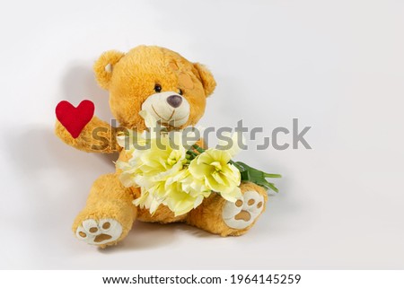 A greeting composition with a funny character in the form of a teddy bear with a bouquet of pale yellow tulips and a red heart  on a light background. The concept of friendship, love and care