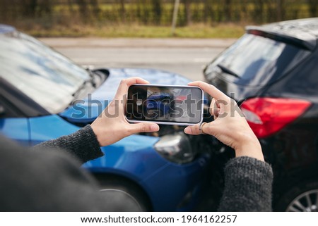 Close up of female driver taking photos of road traffic accident on mobile phone for insurance claim