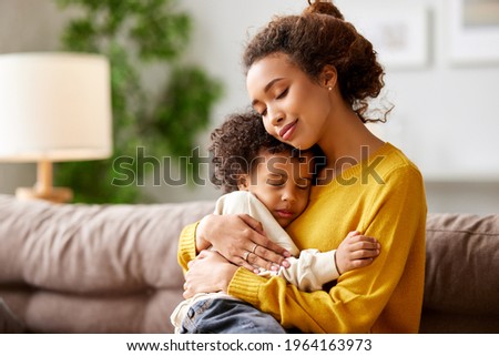 Happy afro american family at home. Young beautiful loving mom with closed eyes embracing cute little kid son while sitting on sofa in living room at home. Mother expressing love to small child Royalty-Free Stock Photo #1964163973