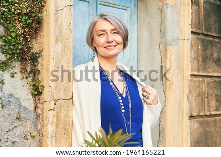 Fashion portrait of beautiful and elegant middle age woman posing outside Royalty-Free Stock Photo #1964165221