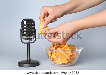 Woman making ASMR sounds with microphone and nacho chip on grey background, closeup
