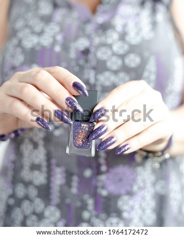 Female hand with long nails and purple lilac manicure holds a bottle of nail polish