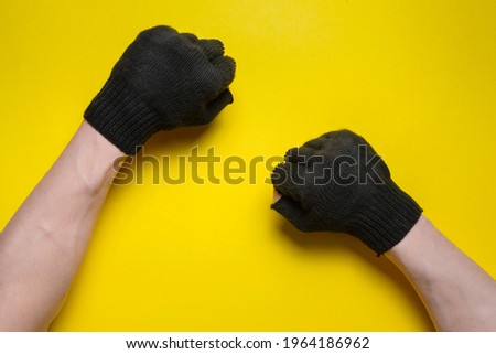 A male hands in the black gardening glove with a clenched fist on the yellow flat lay background.