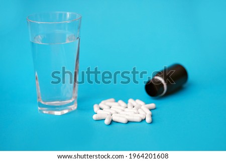 White pills and a glass of water on a blue background. Medical concept of medicines or vitamins for every day. Antibiotics are an irreplaceable aid in medicine