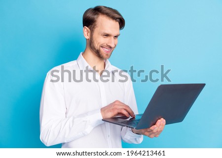 Portrait of attractive cheerful skilled focused man holding in hands using laptop typing isolated over bright blue color background