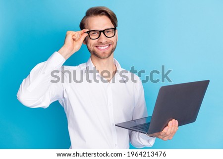 Portrait of attractive cheerful man holding in hands laptop touching specs isolated over bright blue color background