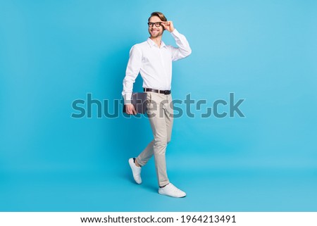 Full body photo attractive positive young man walk smile businessman look empty space hold laptop isolated on blue color background