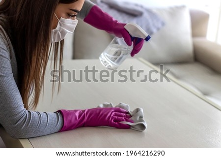 Woman cleaning and polishing the table with a spray detergent at home, housekeeping and hygiene concept. Hands in pink gloves disinfecting kitchen counter and wiping with towel against viruses.