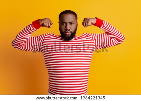 Portrait of strong brutal man show big muscle biceps posing on yellow background