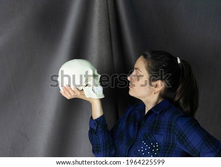 Portrait of a pretty white woman with a skull in her hands, communication and conversation with a skull, dark gray background